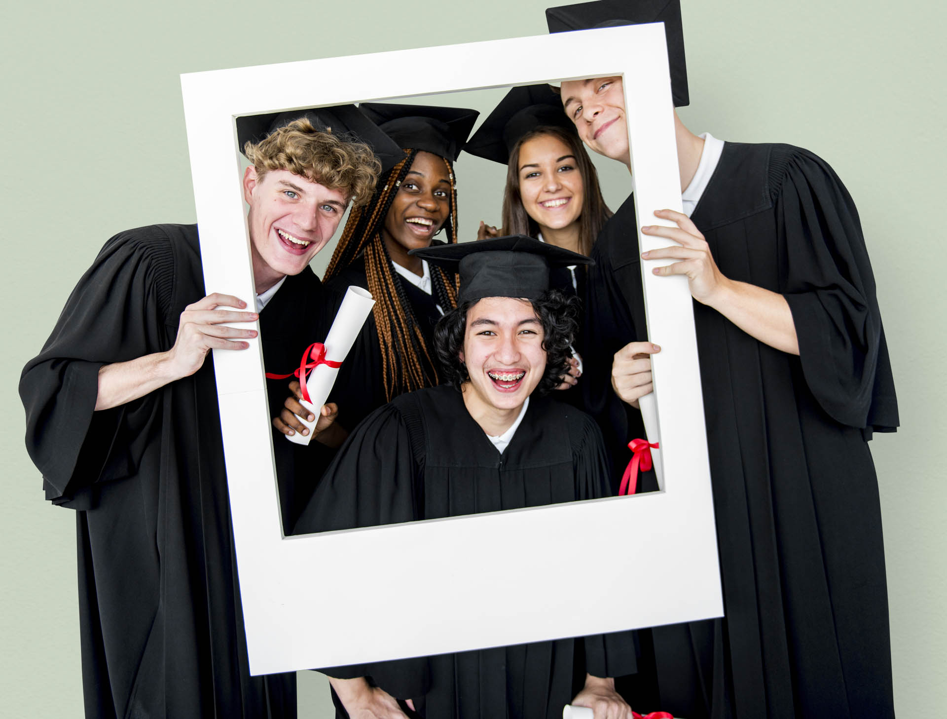 Diverse,Students,Wearing,Cap,And,Gown,Holding,Photo,Frame,Studio